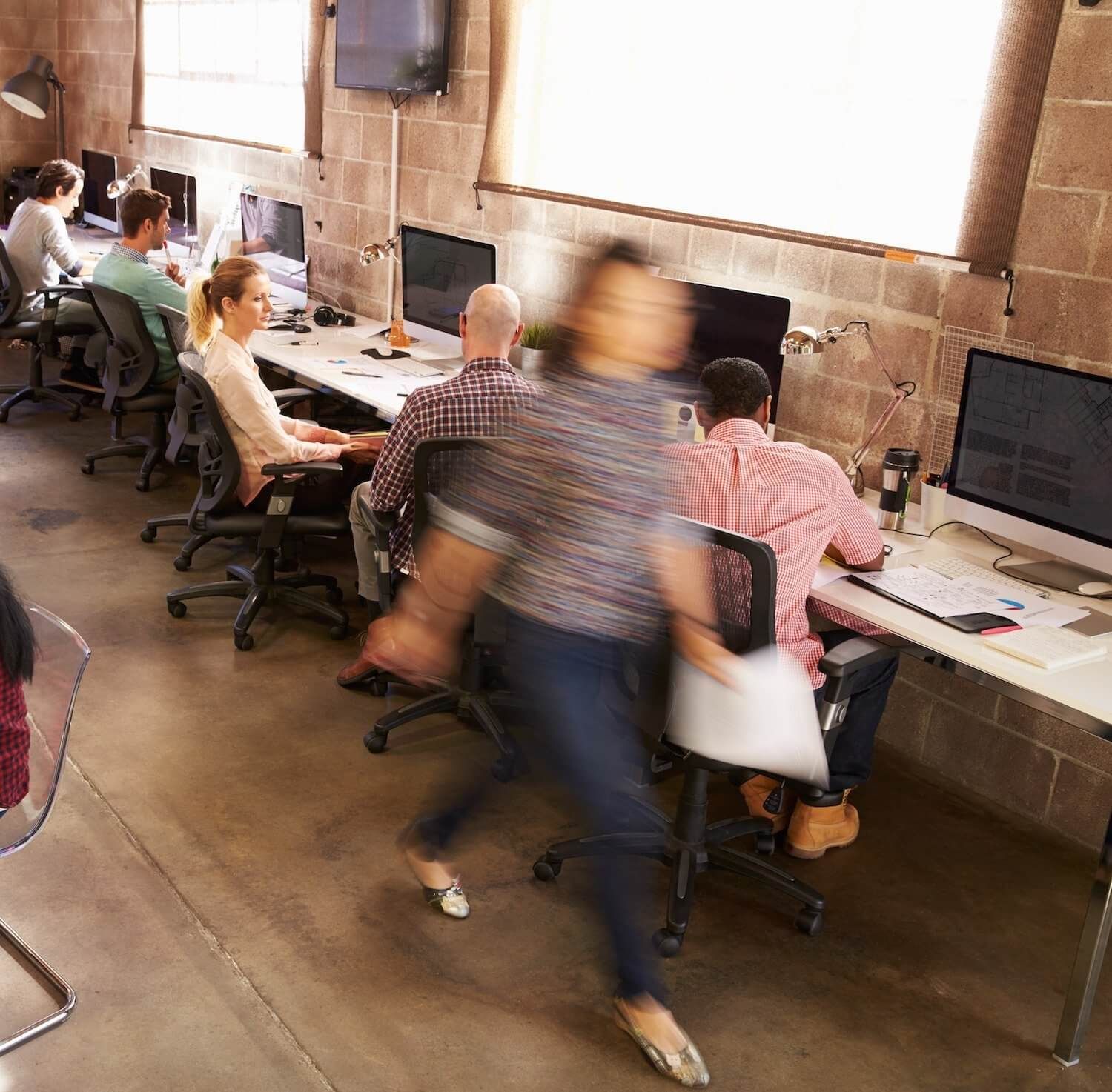 A blurry picture of people sitting at desks in an office