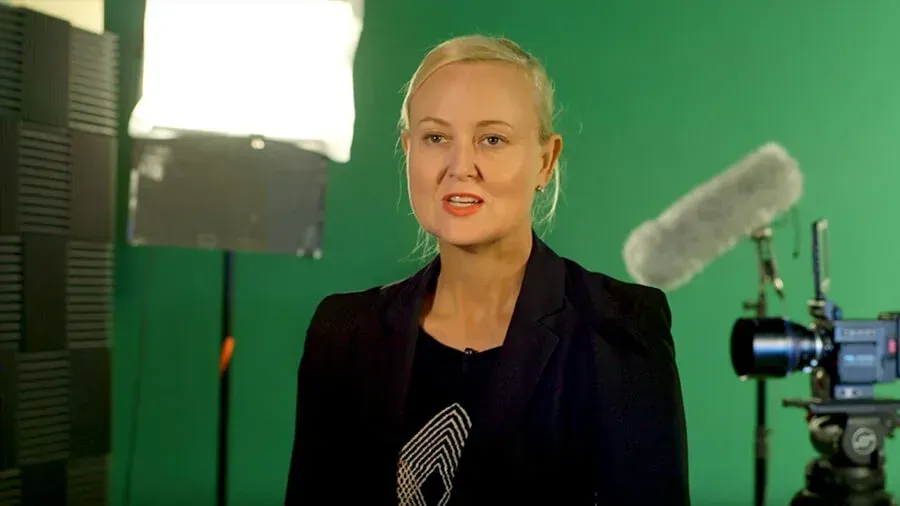 A woman is standing in front of a green screen in front of a camera.