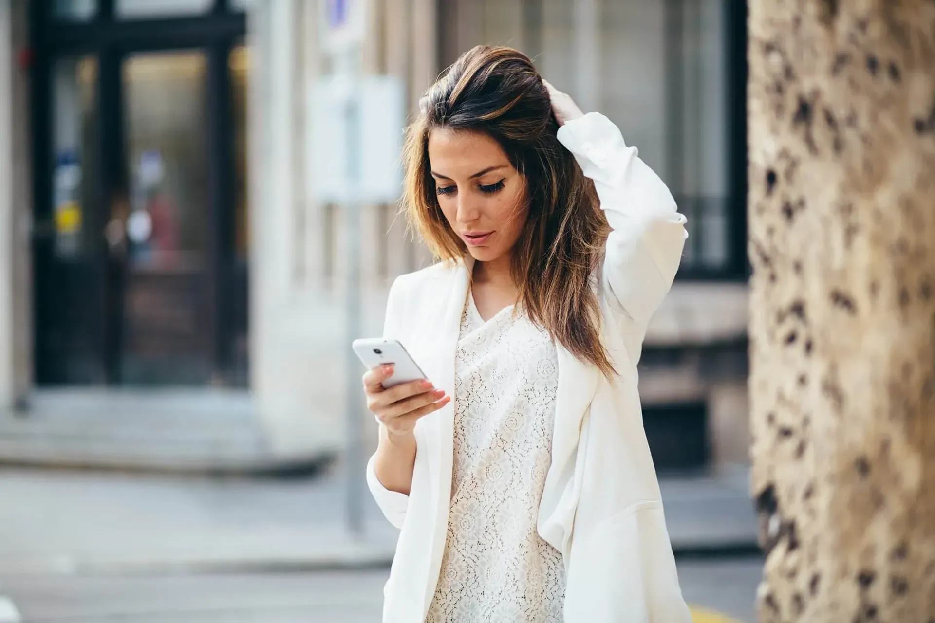 A woman in a white jacket is looking at her cell phone.