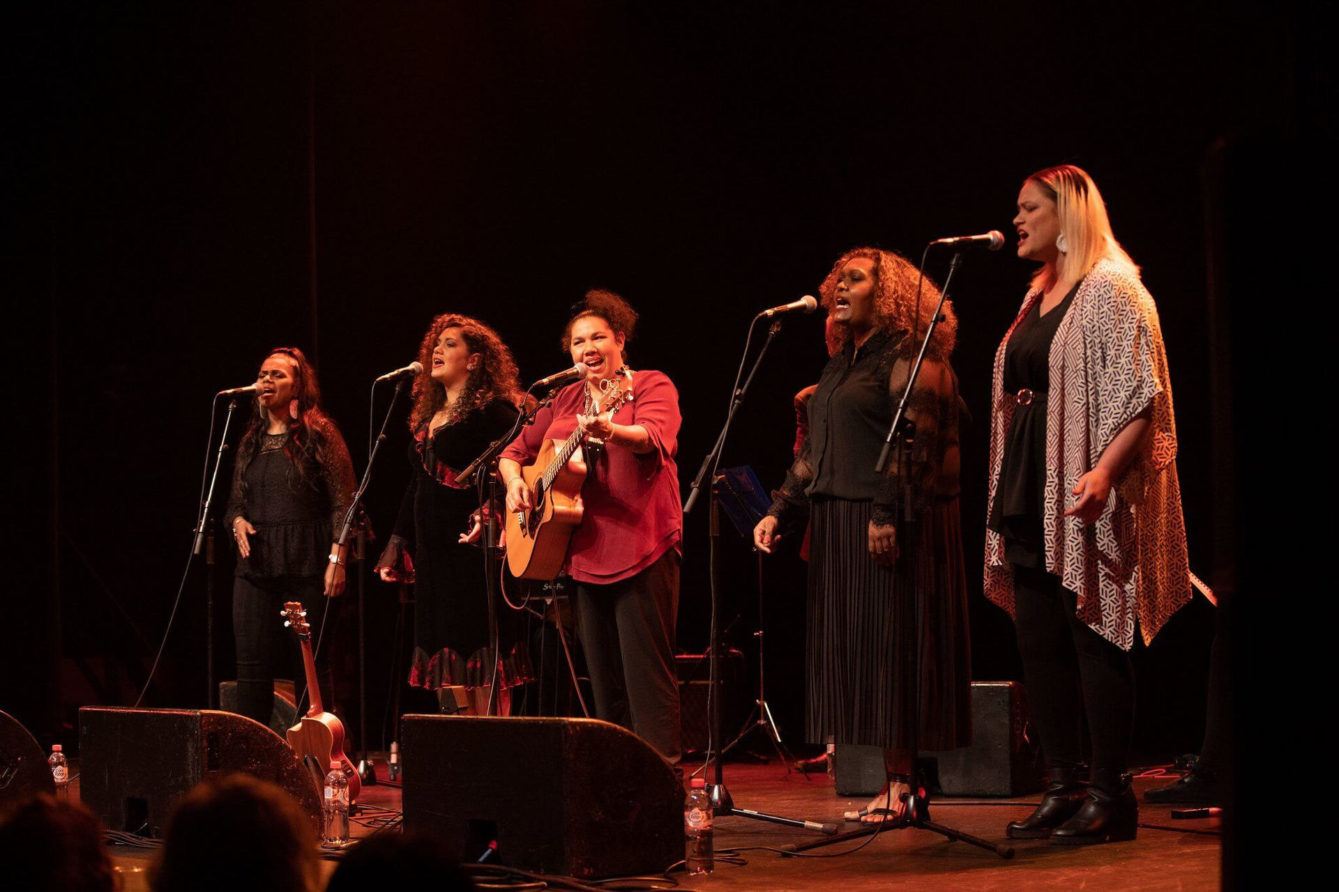 A group of women are singing into microphones on a stage.