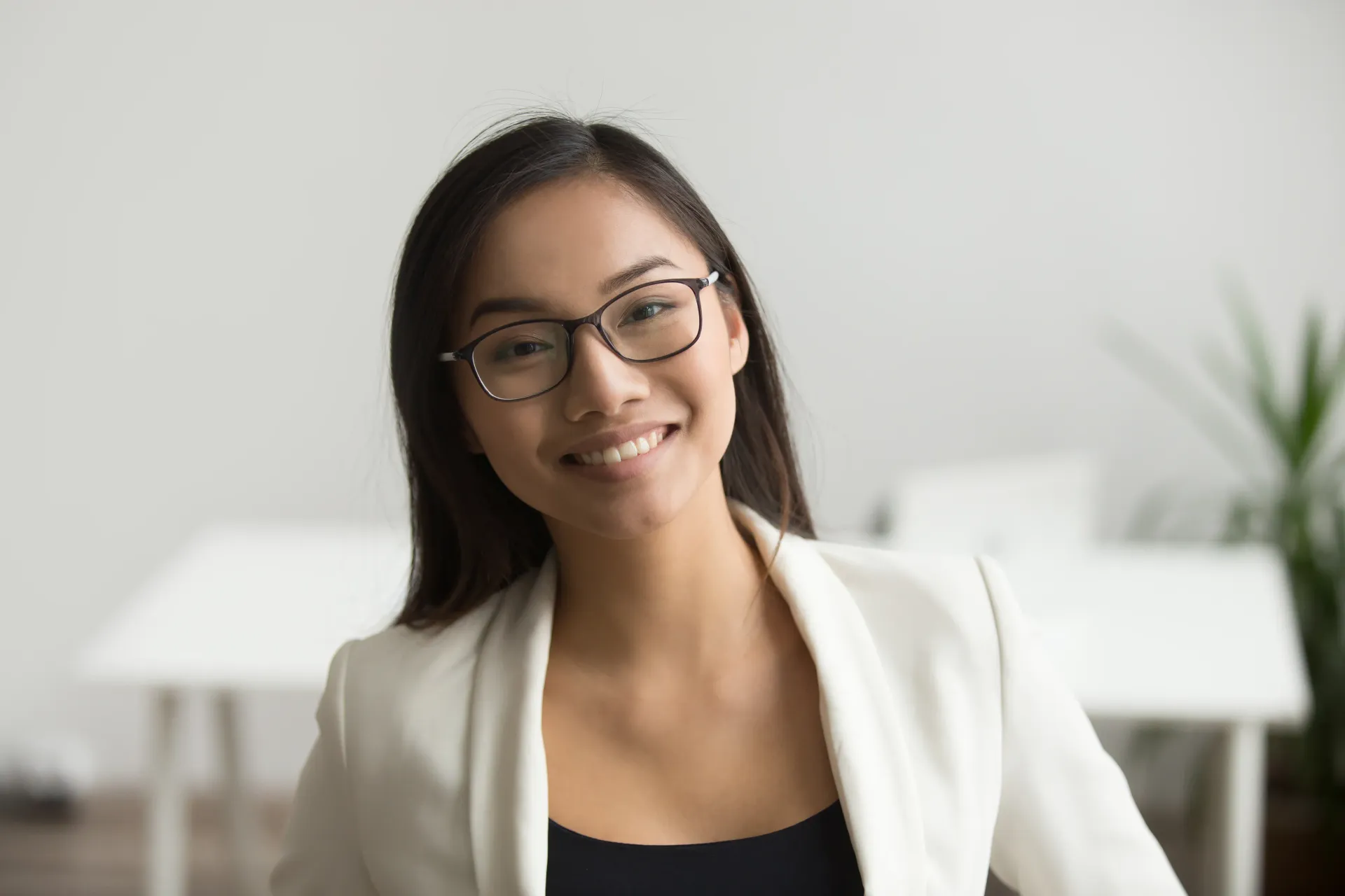 A woman wearing glasses and a white jacket is smiling for the camera.