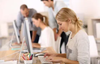 A woman is typing on a keyboard in front of a computer in an office.