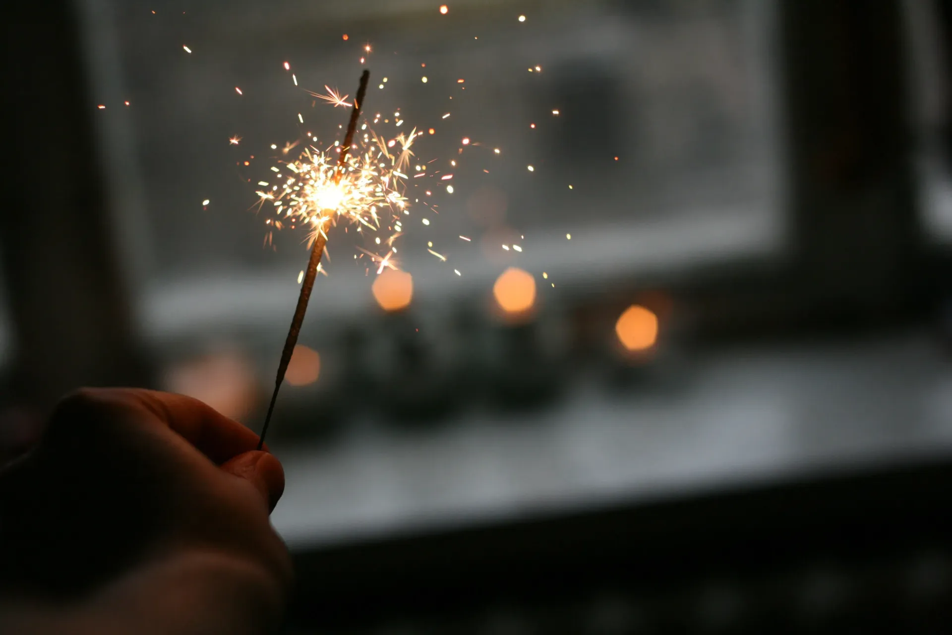 A person is holding a sparkler in their hand in front of a window.
