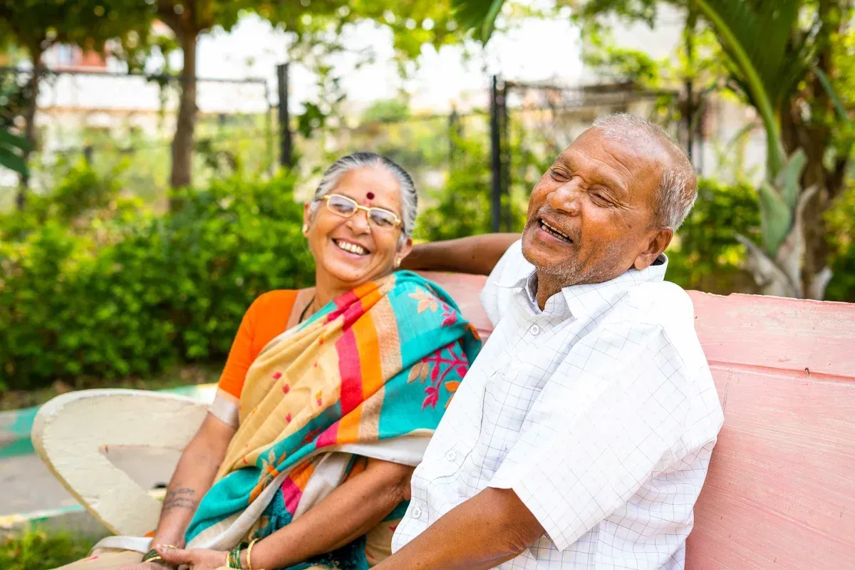 An elderly couple is sitting on a bench in a park.