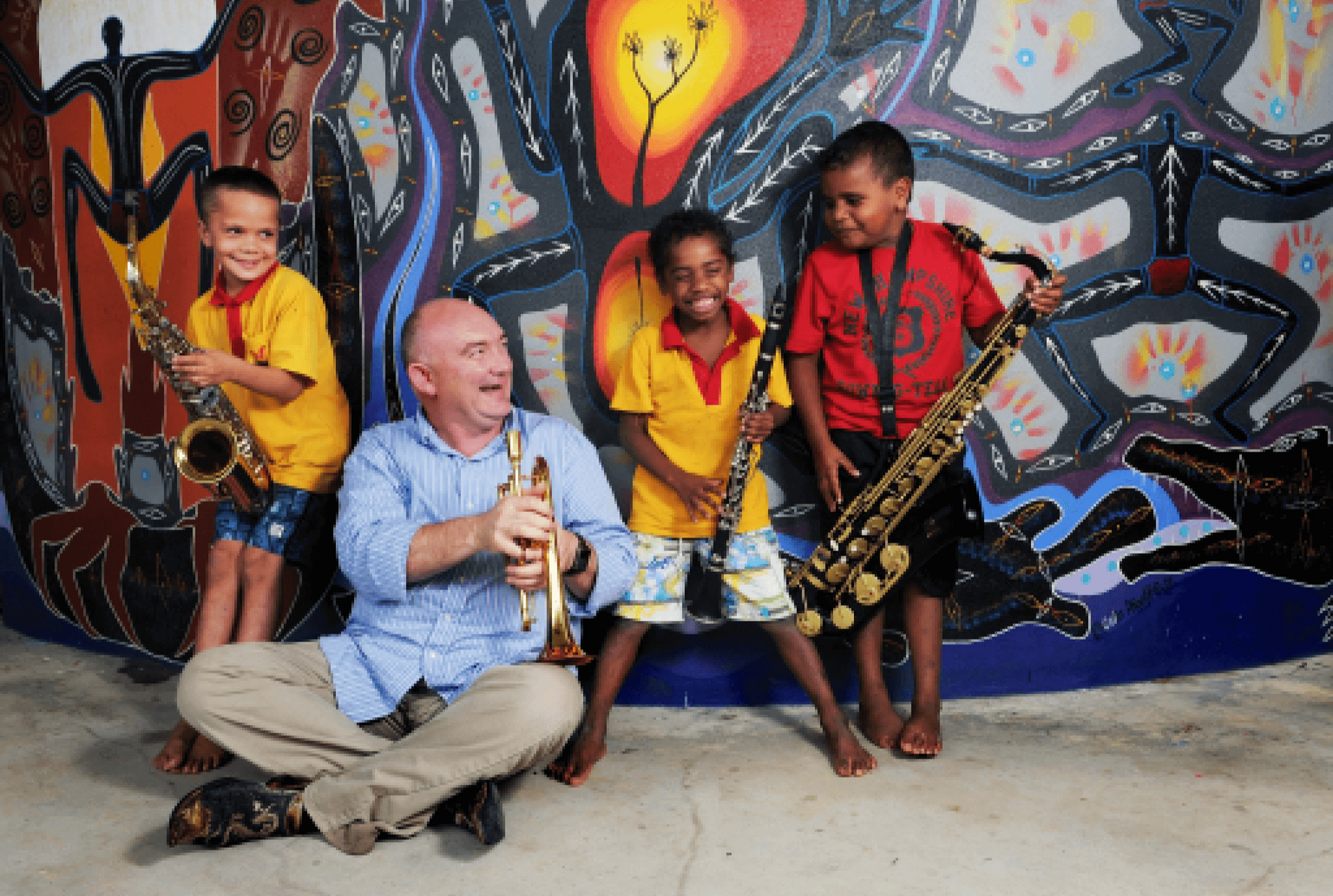 A man playing a trumpet with three children playing saxophones