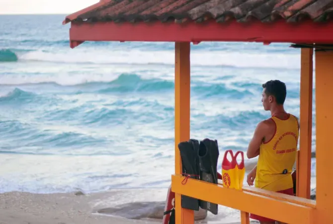 A lifeguard stands in a yellow hut on the beach looking out over the ocean.