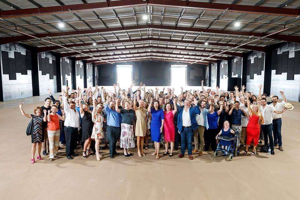A large group of people are posing for a picture in a large warehouse.