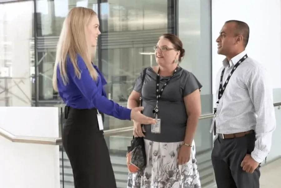 A woman is shaking hands with two other people in a hallway.