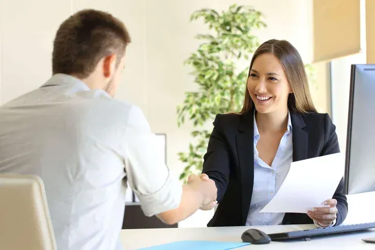 A woman is shaking hands with a man during a job interview.