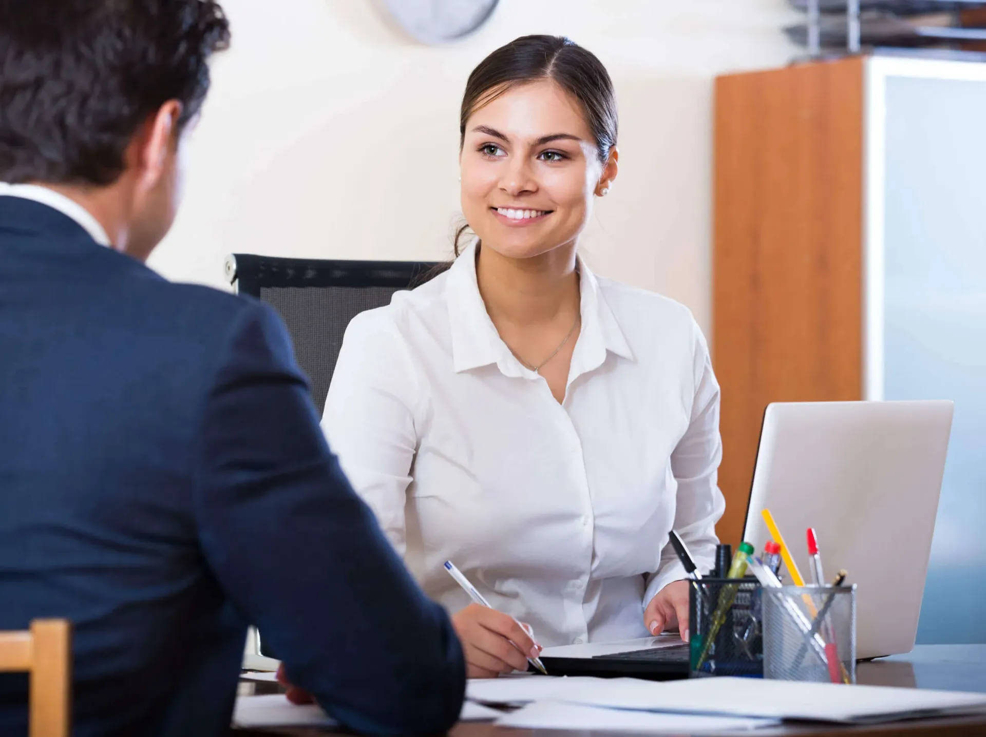 A woman is sitting at a desk talking to a man.