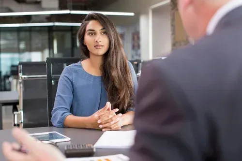 A woman is sitting at a table talking to a man in a suit.