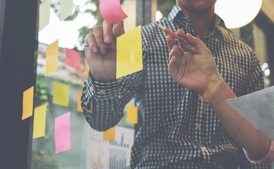 A man is writing on sticky notes on a glass wall.