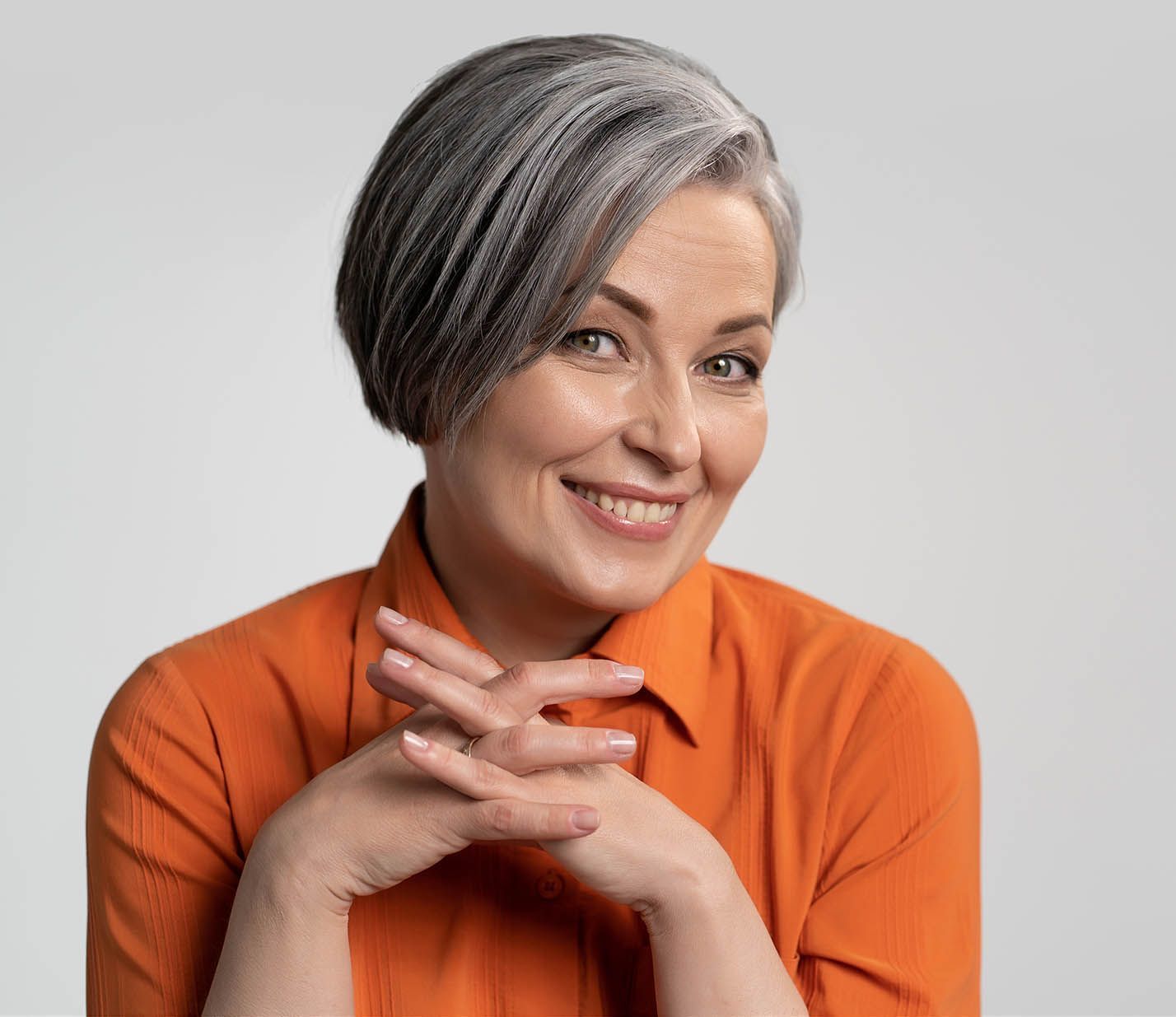 A woman with gray hair is wearing an orange shirt and smiling.