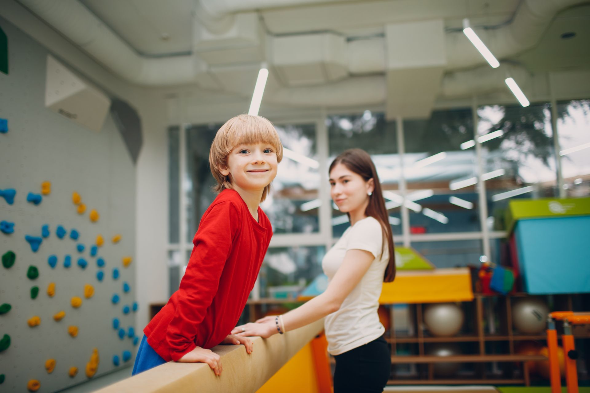 A boy and a girl are standing on a balance beam in a gym.