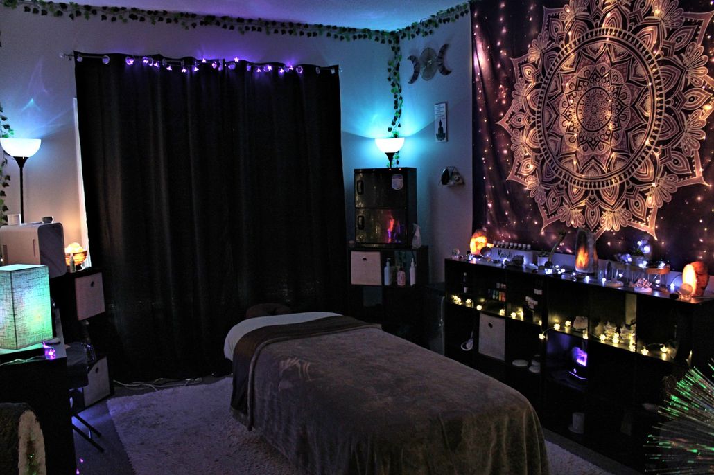 A room with a massage table and a tapestry on the wall.