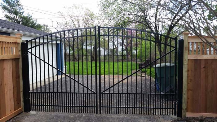 A decorative black wrought iron gate with floral accents set between two light-colored pillars in front of a house.