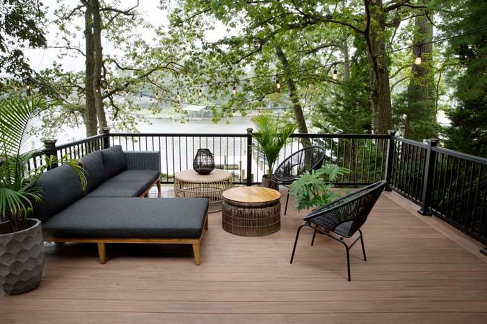 A wooden deck seating area with built-in benches, glass railings, and glowing step lights at sunset.