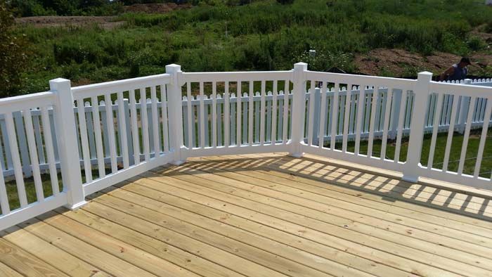 A person wearing work gloves uses a cordless drill to fasten a metal bracket onto a wooden deck railing outdoors.