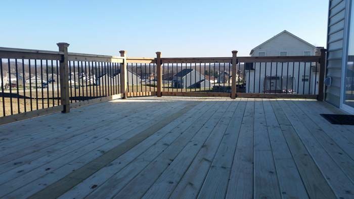 A low-level wooden deck with a simple railing stands in a backyard with green grass and a wooden fence.