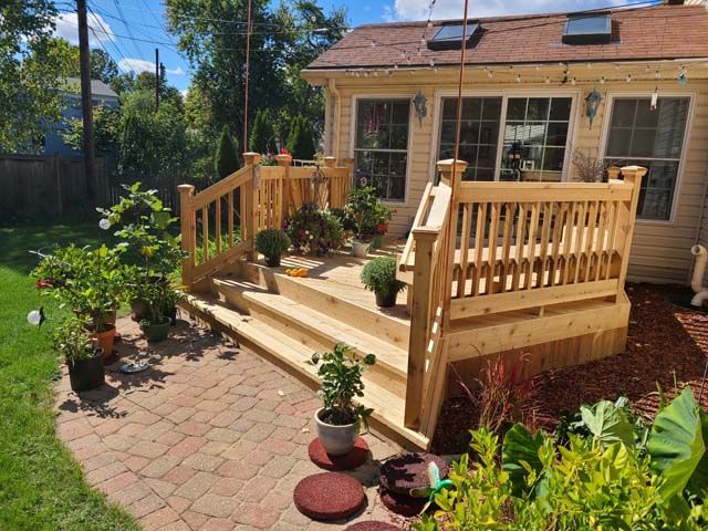 A family relaxes on a wooden patio deck featuring outdoor furniture, a table, and potted plants in a backyard.