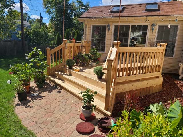 A wooden patio deck with a dining table, four chairs, and a separate armchair outside two gray houses.