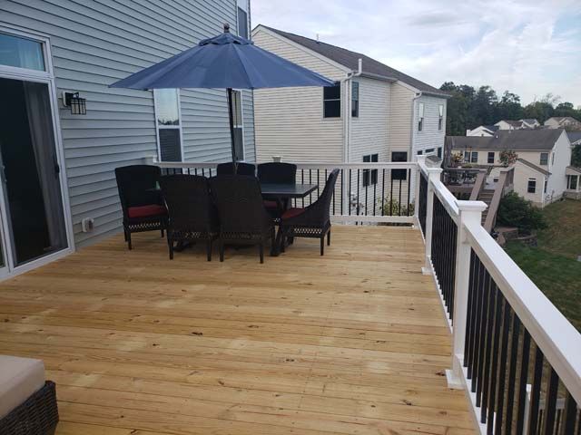 A brown wood deck with stairs and railing attached to the back of a house, featuring outdoor patio furniture.