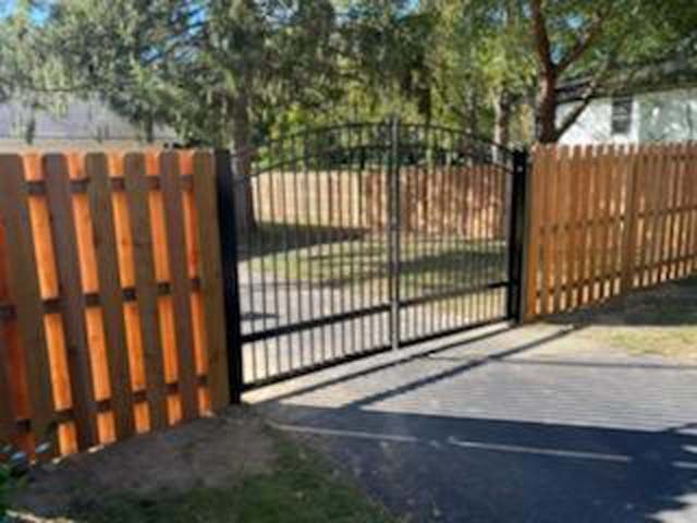 A selection of fence panels, including metal, wood, and vinyl options, leaning against a wooden picket fence in grass.