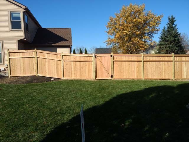 Three construction workers in hard hats and safety gear build a wooden fence outdoors.