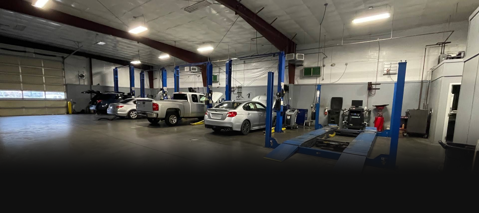Inside a car repair shop: vehicles on lifts, tools and equipment, bright overhead lights.