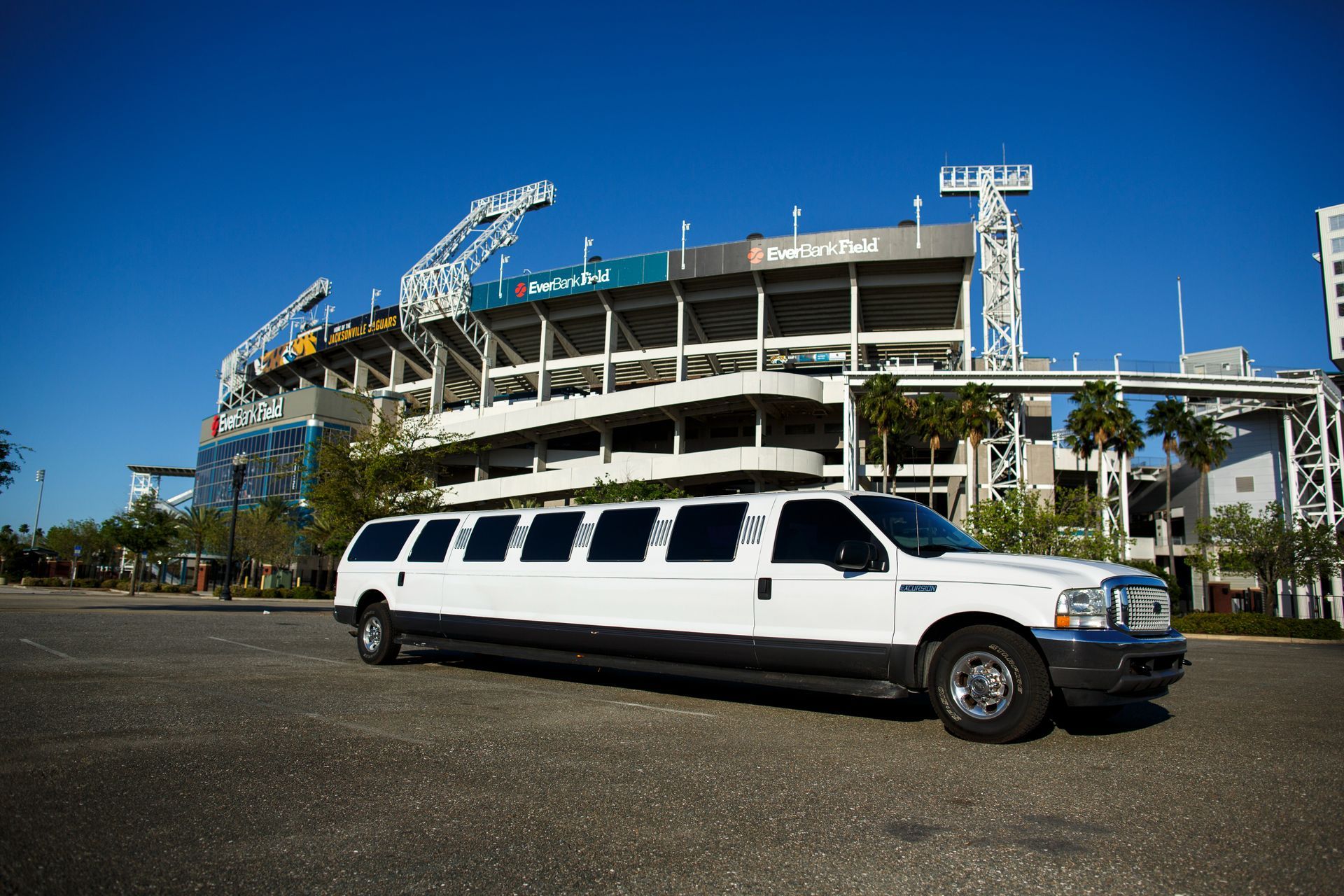 White stretch limousine parked outside a baseball stadium under a blue sky