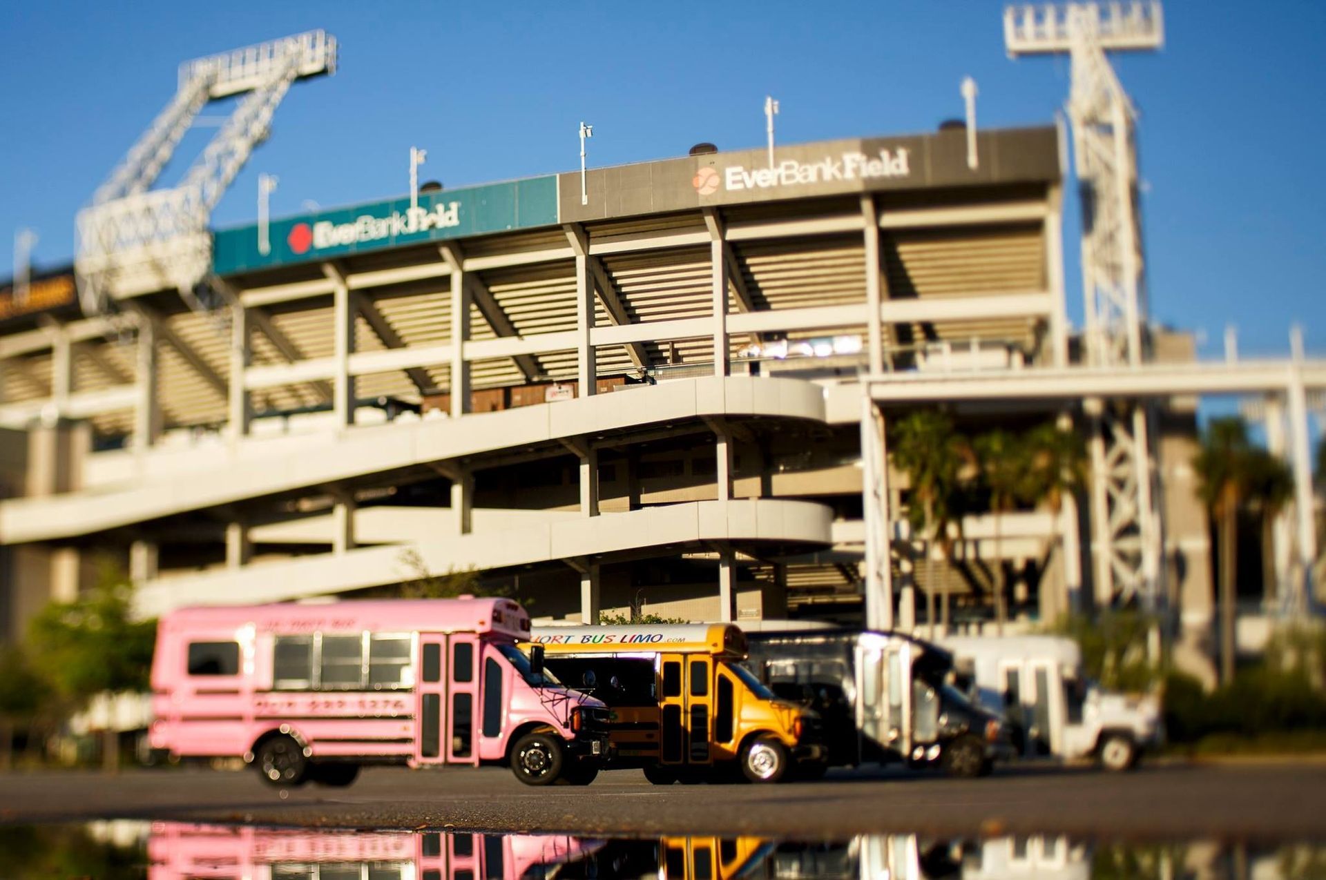 Pink and yellow buses parked outside a stadium with metal stairs and signage on top