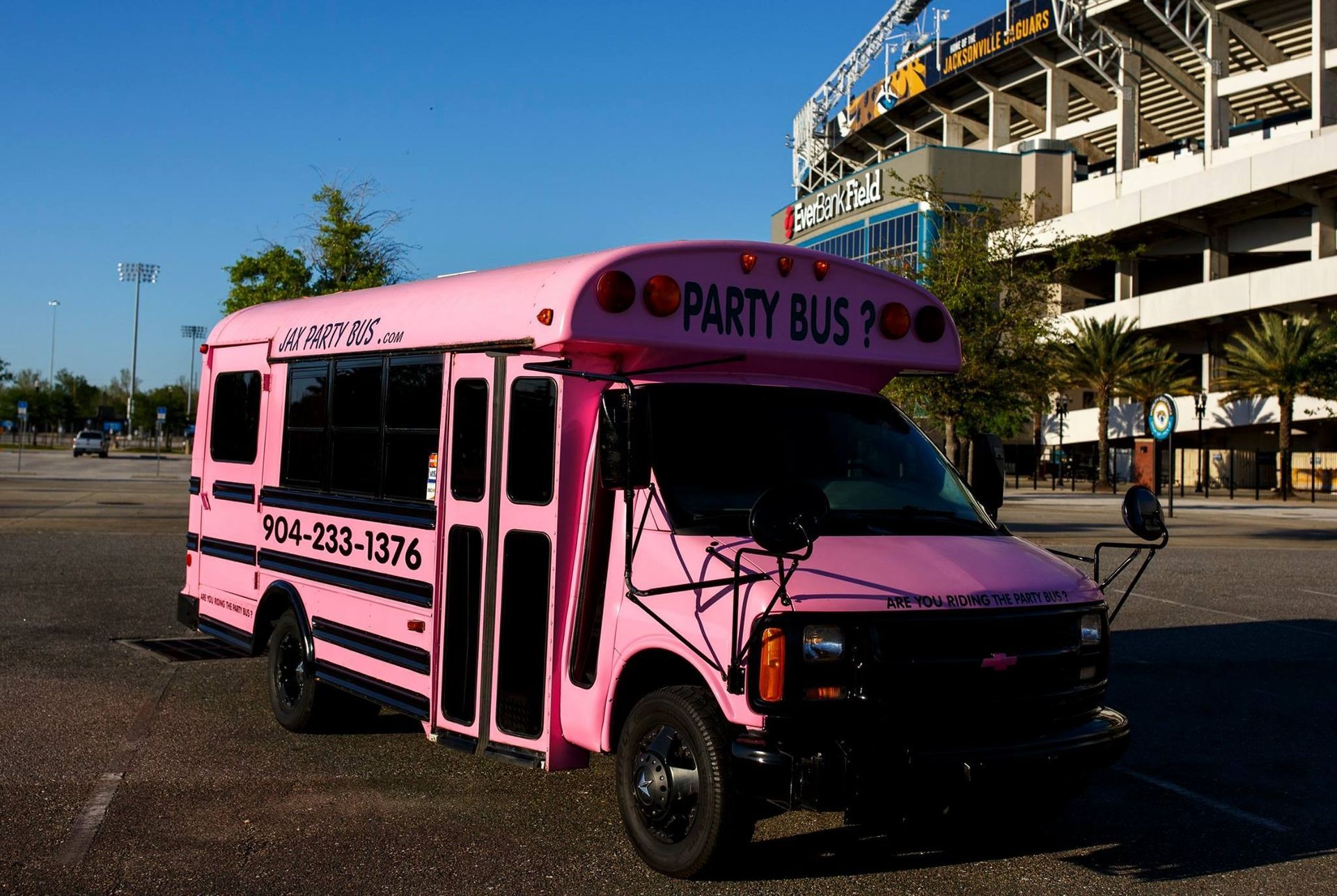 Pink party bus parked outdoors near a stadium