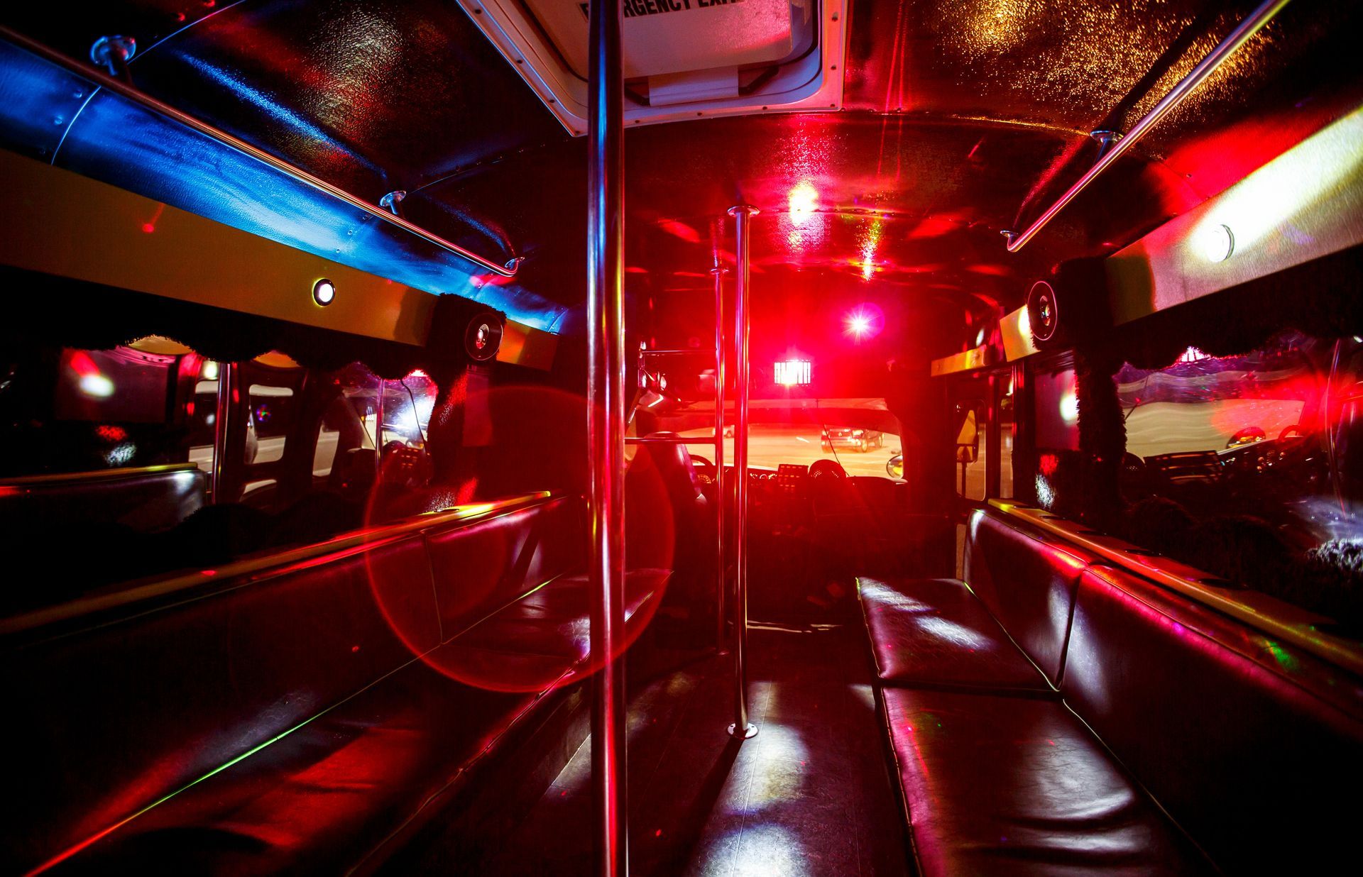 Red-lit interior of a bus or train at night, with empty seats and metal poles reflecting city lights.