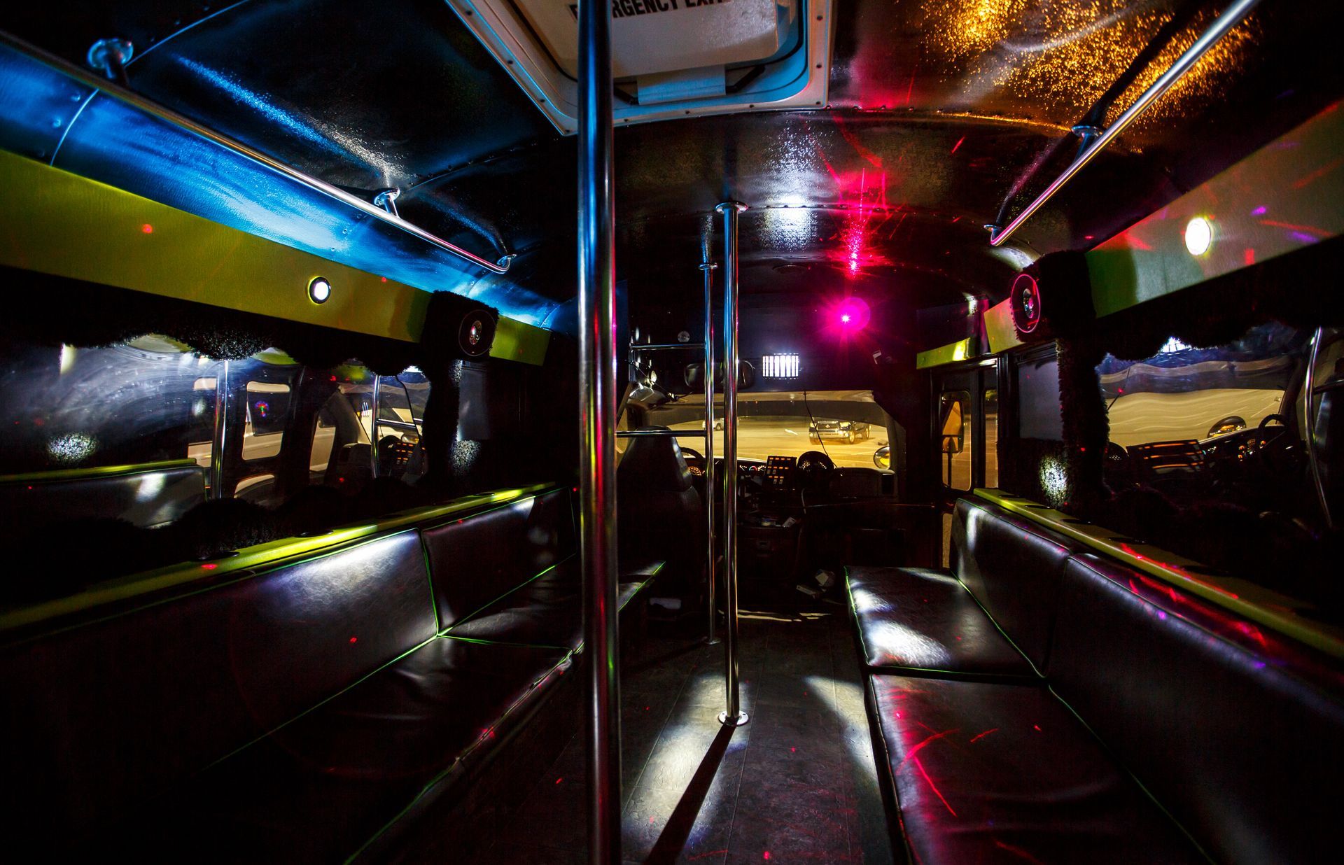 Dim, colorful interior of a bus or tram at night with reflective metal seats and lights.