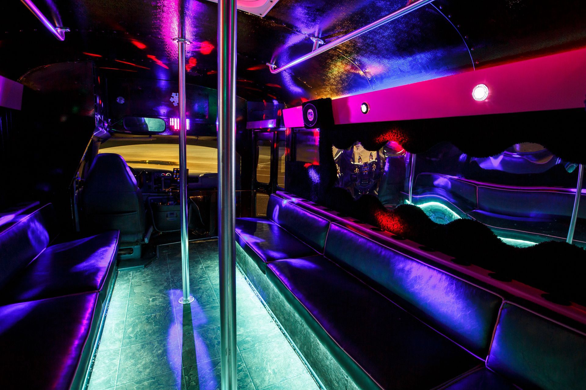 Neon-lit party bus interior with purple and green lights, mirrored poles, and bench seating