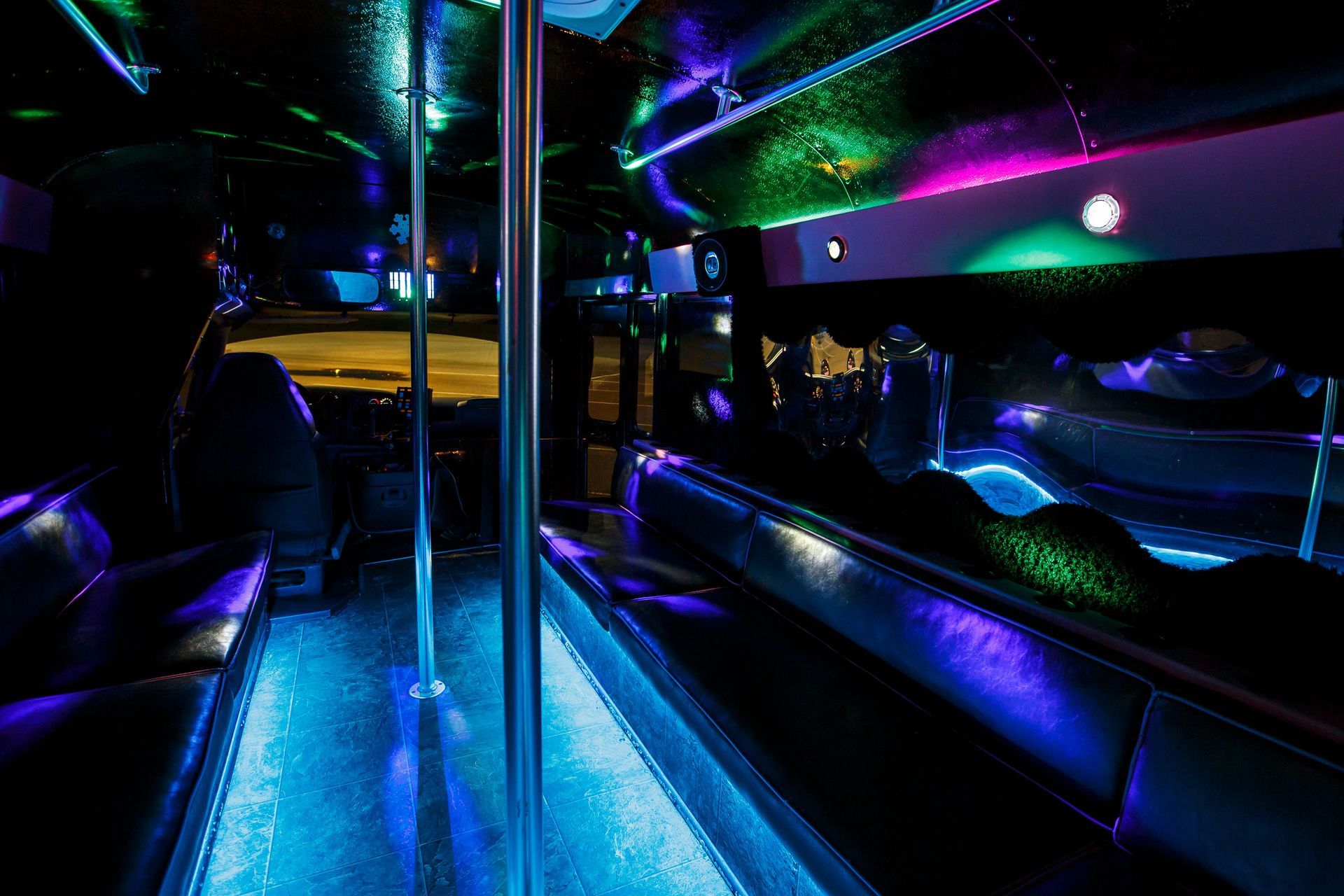 Neon-lit bus or limo interior with blue floor lights, dark leather seats, and colorful ceiling lights