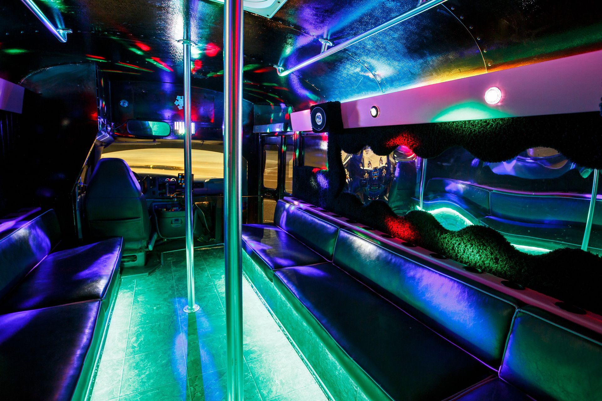 Neon-lit party bus interior with colorful LED lights, black seats, and a mirrored dance pole