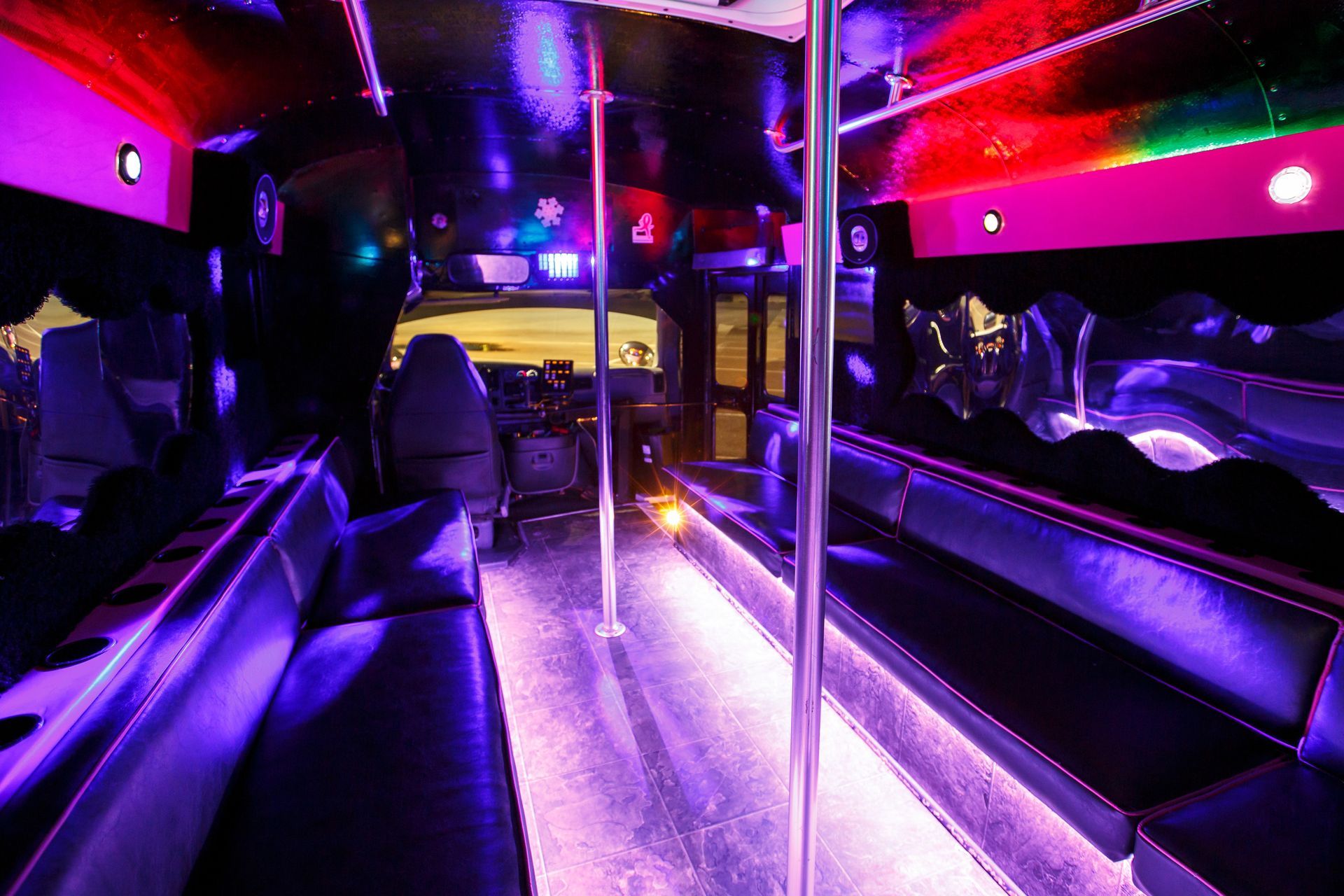 Purple-lit party bus interior with black seats, chrome poles, and a glowing aisle