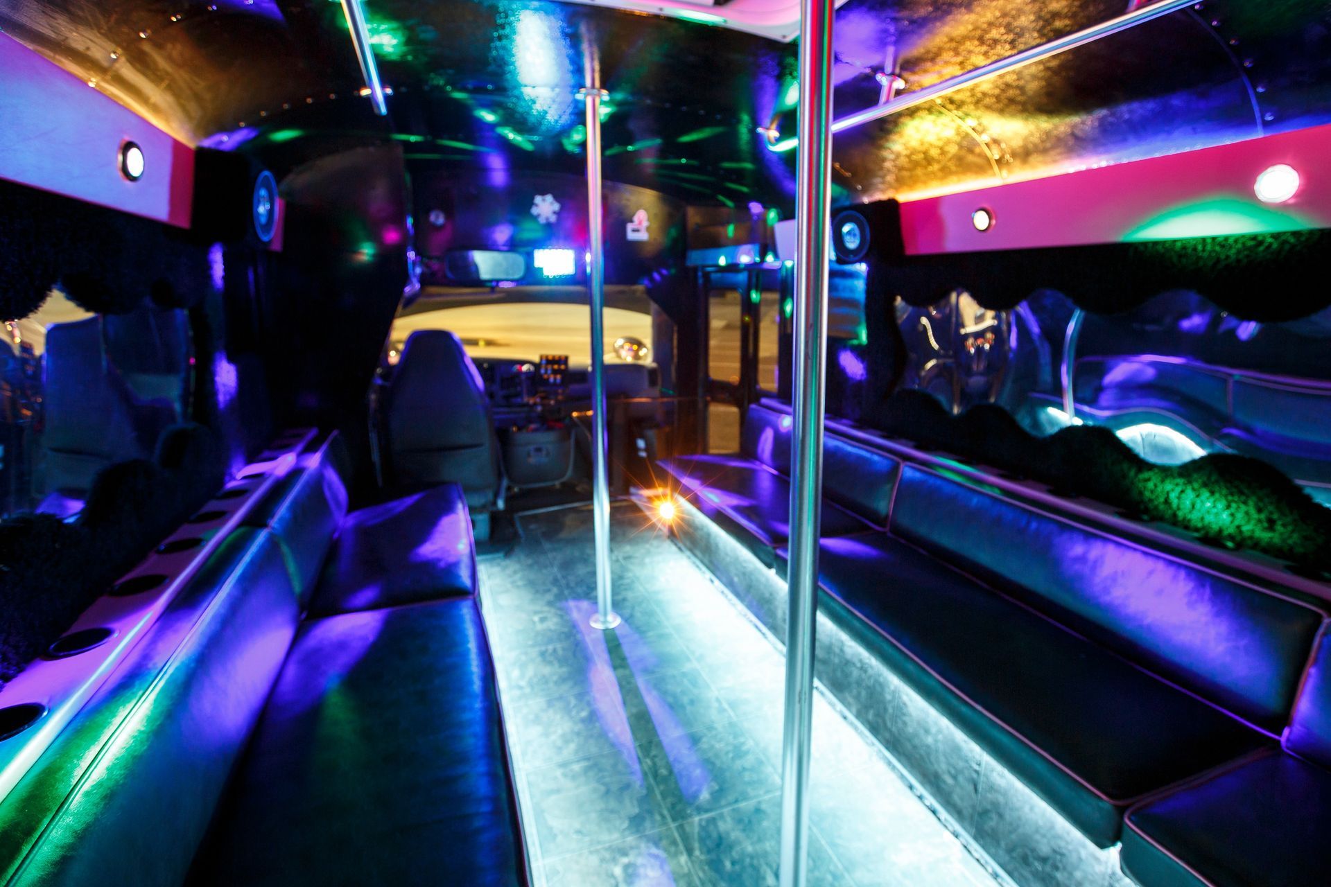 Inside a neon-lit limousine with mirrored walls and purple-blue lighting, showing leather seats and a central pole.
