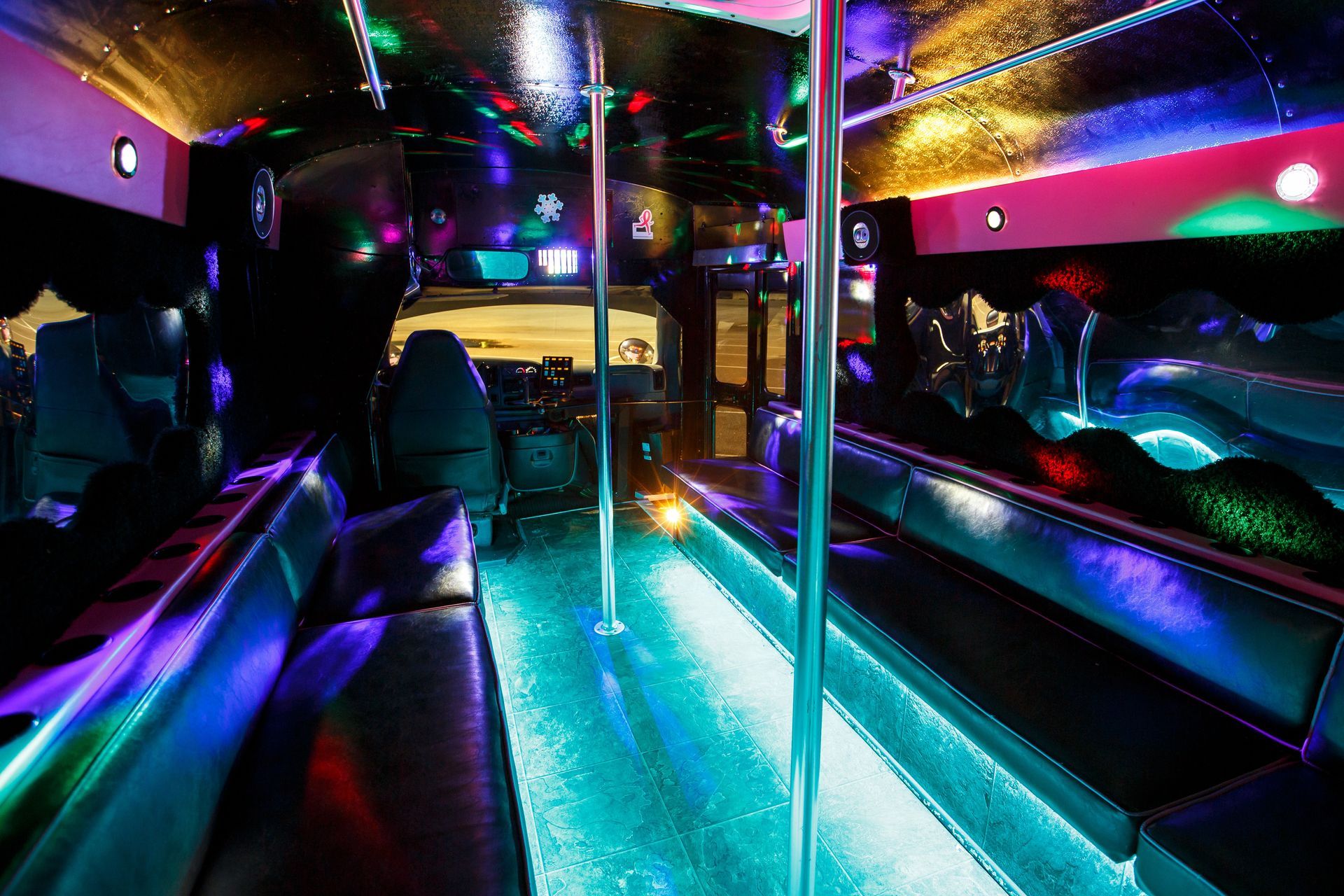 Neon-lit party bus interior with mirrored walls, colorful lights, and a shiny center pole