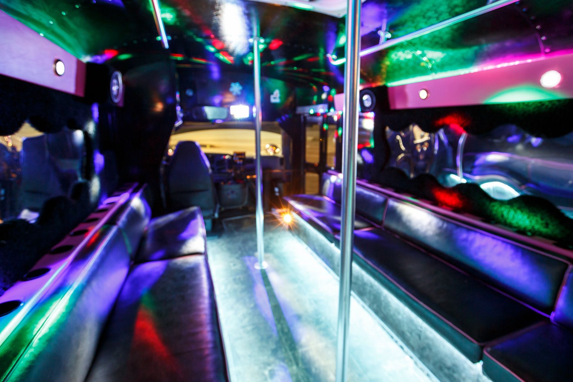 Inside a neon-lit party bus with mirrored walls, benches, and colorful lights reflecting on the floor.