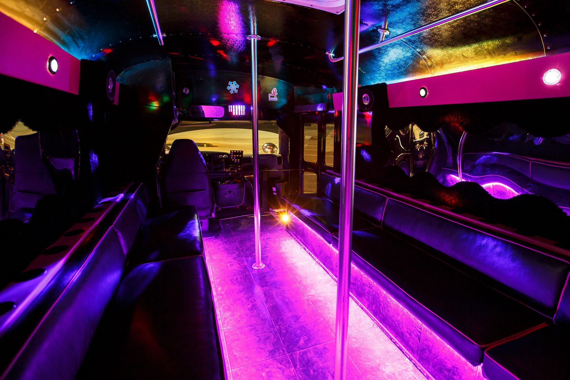 Empty party bus interior with pink and purple neon lighting, shiny floor, and seated booths on both sides