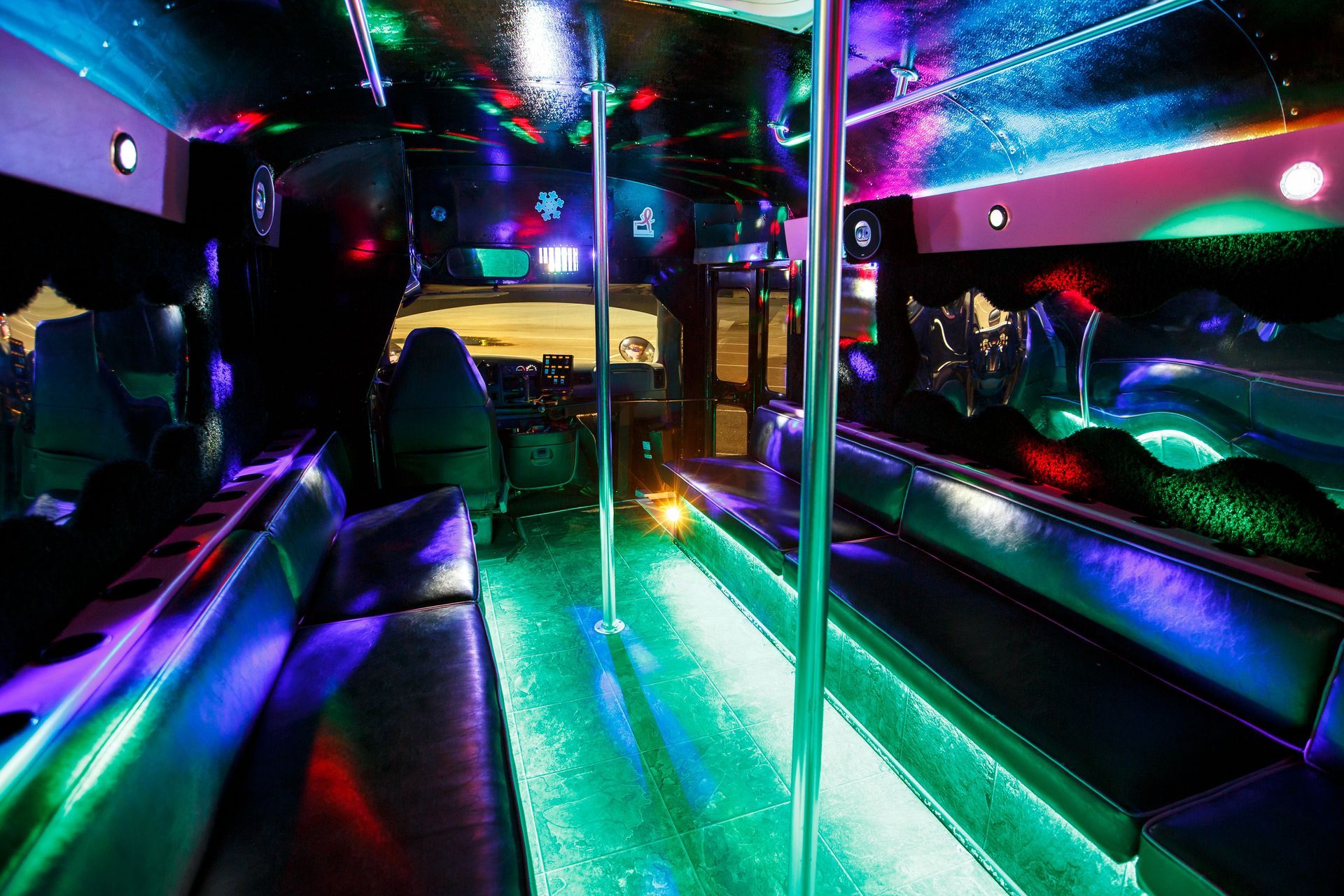 Neon-lit party bus interior with colorful lights, mirrored walls, and leather bench seating