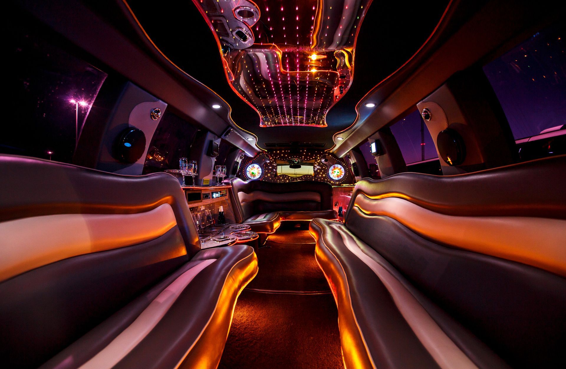 Neon-lit luxury limo interior with orange lighting, curved white seats, and mirrored ceiling