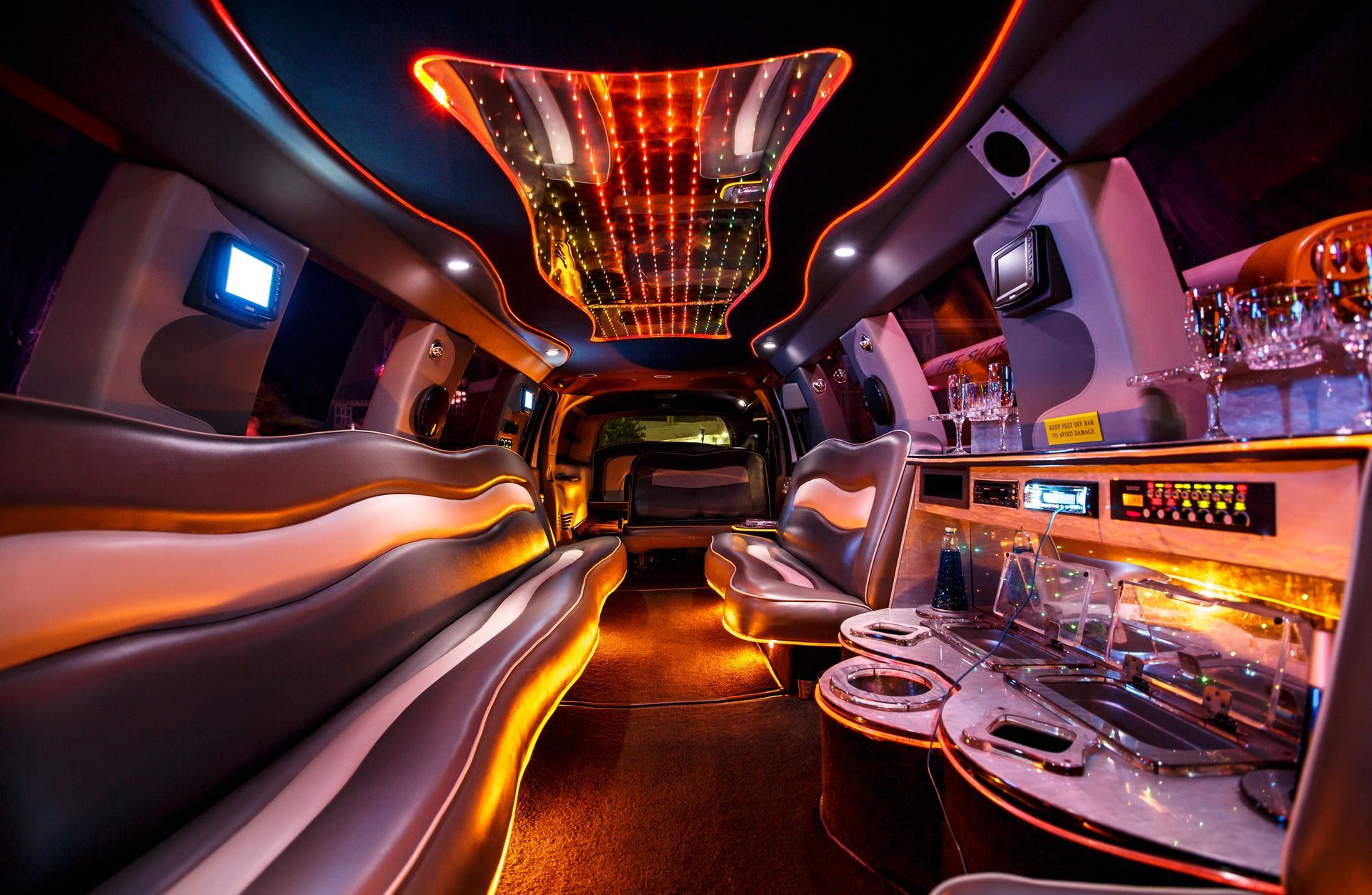 Luxurious party bus interior with neon orange lighting, leather seats, and a chrome bar area