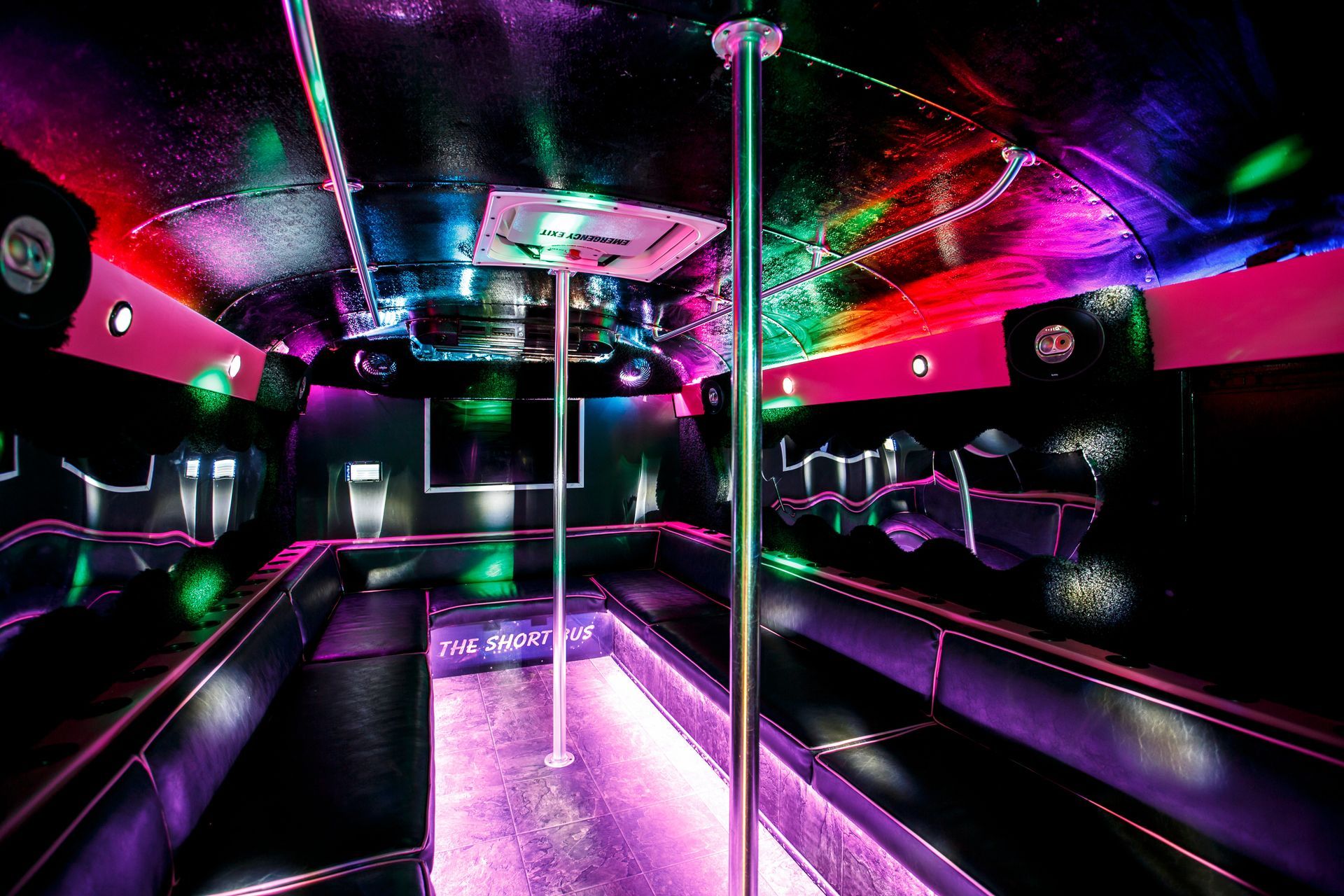 Neon-lit nightclub interior with purple and pink lights, mirrored walls, and a central dance pole