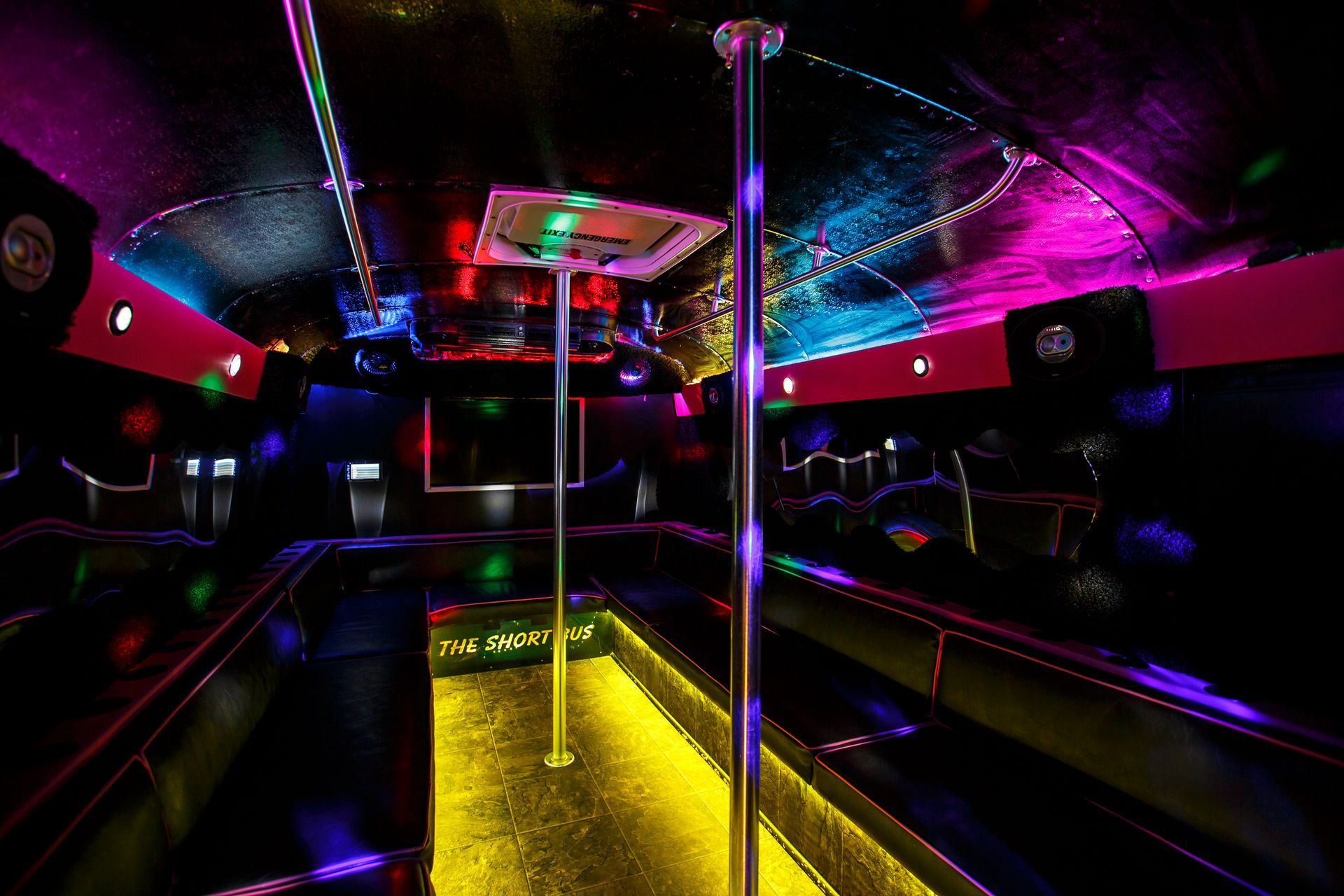 Neon-lit bus interior with glowing yellow floor, chrome poles, and pink-purple reflections.