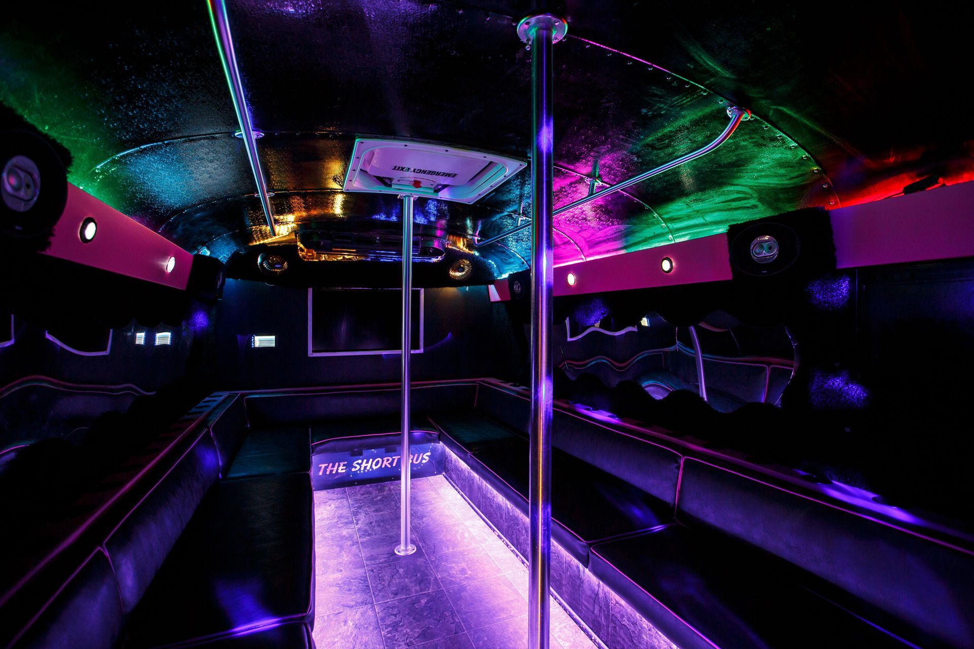 Neon-lit party bus interior with purple floor lights, pole, and colorful ceiling lights