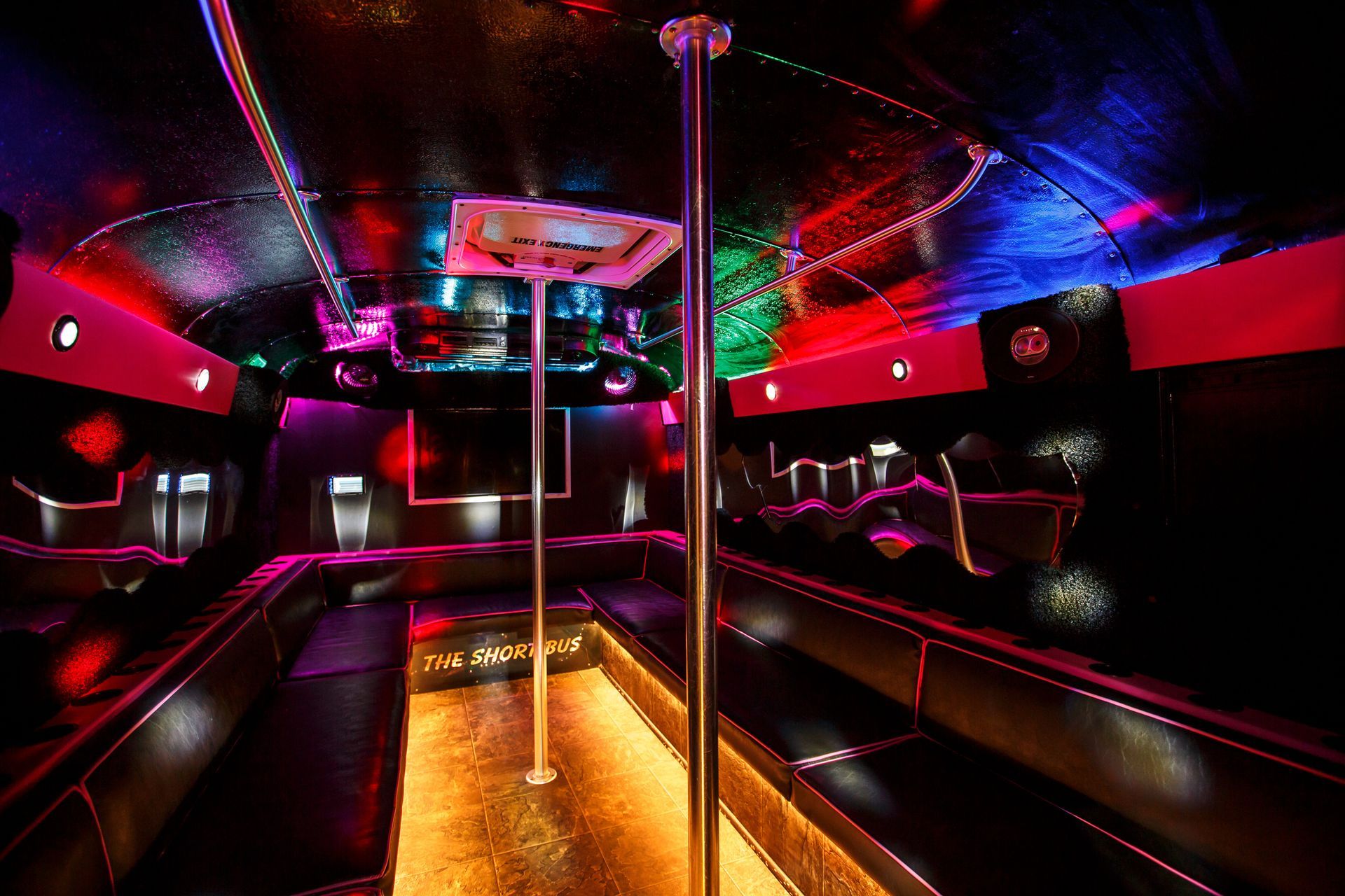 Neon-lit party bus interior with dance pole, red seats, and colorful ceiling lights