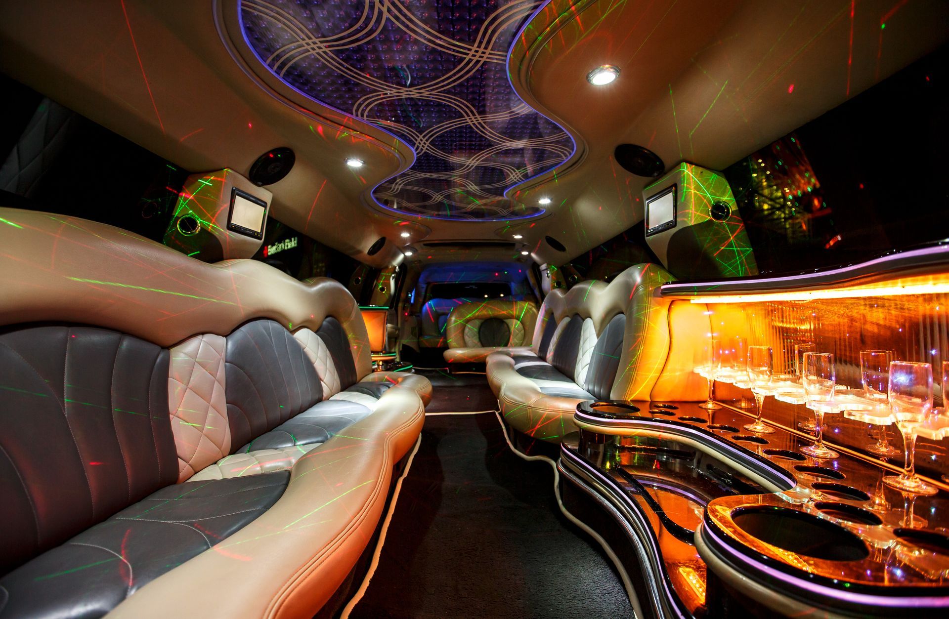 Luxury limousine interior with leather seats, neon ceiling lights, and glowing bar area at night